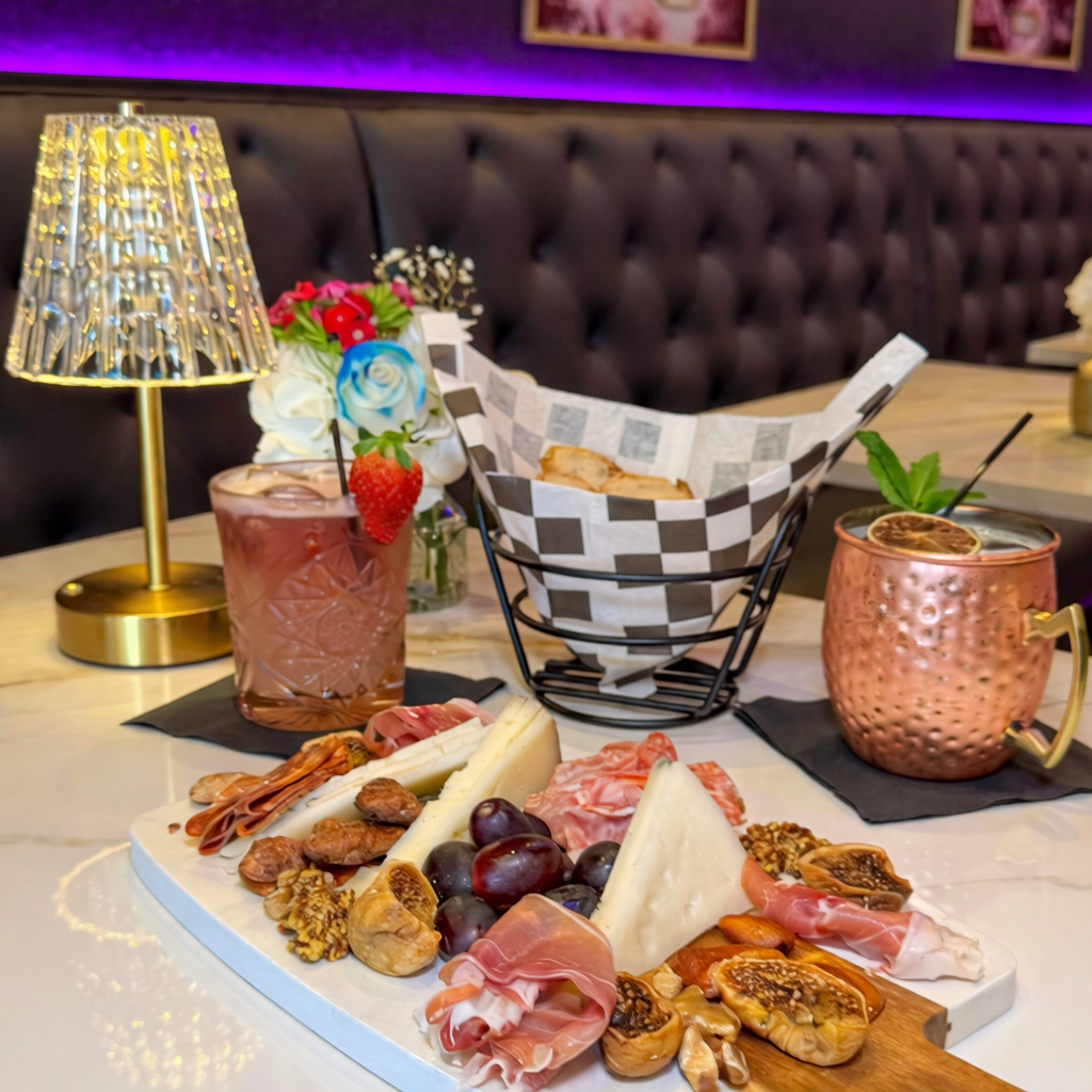 Charcuterie board with prosciutto, cheeses, figs, and grapes alongside cocktails at Babe Coffee Lounge
