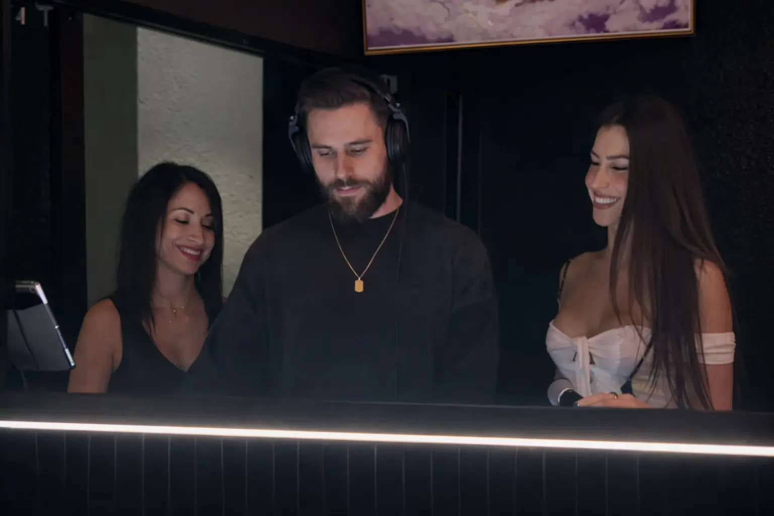 Two guests smile beside a DJ in headphones at the Babe DJ booth